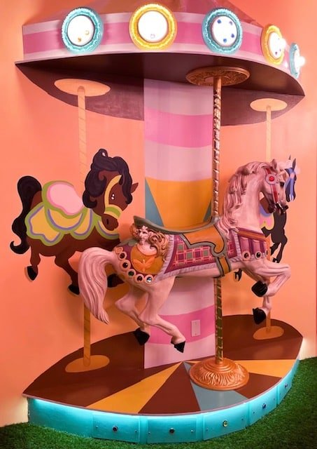 An image of the Carnival escape room at Escape This Frederick. The image shows a carousel with horses with bright colors and lights.