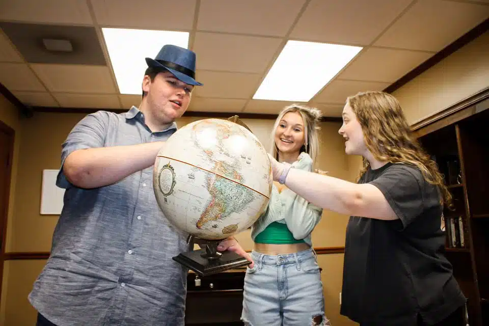 An image of the Mob Boss escape room. Three players seem excited while looking at a globe and attempting to solve puzzles.
