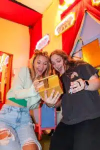 An image of The Carnival escape room at Escape This Frederick. Two girls are seem surprised and excited to open a golden box.